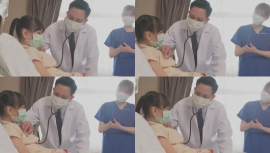 亚洲医生在康复室的床上用听诊器测量小孩的心率。冠状病毒大流行期间，戴口罩的男女检查女童。年轻的护士和孩子说话。高清在线视频素材下载