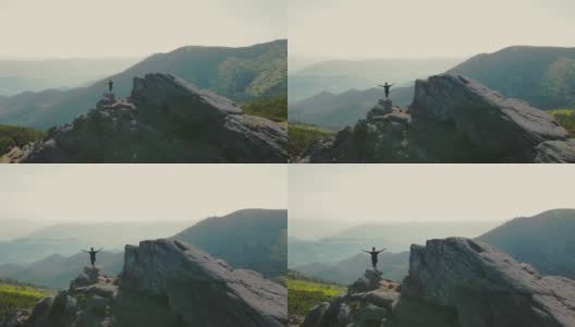 一个徒步旅行者站在一块岩石上，在日落时展望未来。运动员站在山顶眺望远方。从后面鸟瞰一个圆圈高清在线视频素材下载