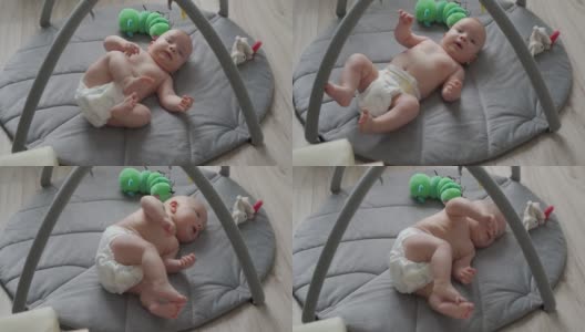 可爱的3个月的小男孩学习从他的背部到腹部，当他躺在游戏垫上，婴儿活动在婴儿游乐场的软垫上。高清在线视频素材下载