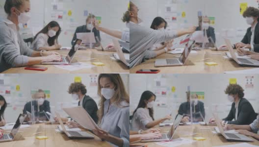 2019冠状病毒病大流行期间，一群戴着防护口罩的商务人士坐在银行办公室的办公桌前，戴着防打喷嚏装置，使用电脑高清在线视频素材下载