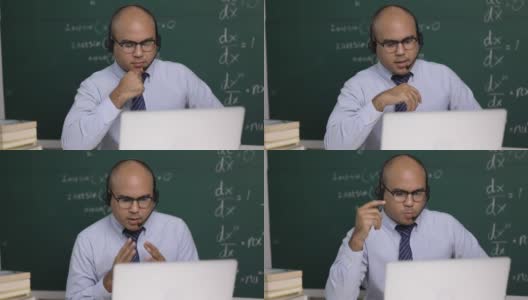 印度年轻教师男子戴着耳机坐着用笔记本电脑进行在线视频会议直播。亚洲数学教师在线授课，供学生在线学习。高清在线视频素材下载
