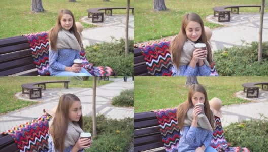 美丽的女孩坐在长椅上，在一个阳光明媚的秋天公园。女孩在户外喝着热咖啡。秋天日落时，年轻的黑发女子坐在长凳上高清在线视频素材下载