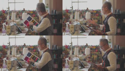 亚洲华人高级男子在他的工作室展示变化纺织品织物样本目录视频电话客户与数字平板电脑高清在线视频素材下载