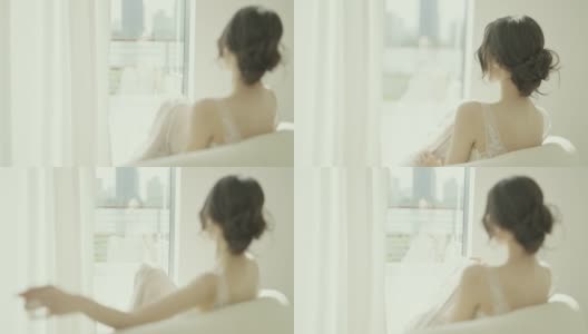 身穿白色婚纱的美丽亚洲新娘坐在落地窗前的沙发上慢镜头拍摄高清在线视频素材下载