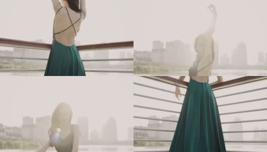 一位身穿绿色晚礼服的年轻亚洲新娘，站在湖滨码头，以城市建筑为背景，微笑着看着镜头，用慢镜头拍摄高清在线视频素材下载
