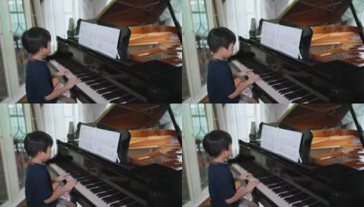 亚洲男孩在客厅里弹三角钢琴，看着音符。孩子专心练习。业余爱好和在家学习。快乐的一天和家庭的概念。活动和生活方式。高清在线视频素材下载