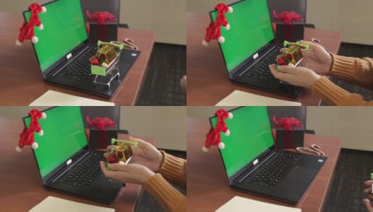 在绿色屏幕和圣诞装饰背景的笔记本电脑键盘上，年轻女性的手拿着装满小礼物的购物车。交付的概念。模拟的内容高清在线视频素材下载