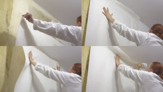 一个女人在房间里修理，用胶水把墙壁涂得乱七八糟，然后贴上白色的墙纸高清在线视频素材下载