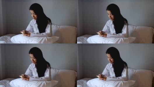 年轻的亚洲女性躺在床上使用智能手机或平板电脑高清在线视频素材下载