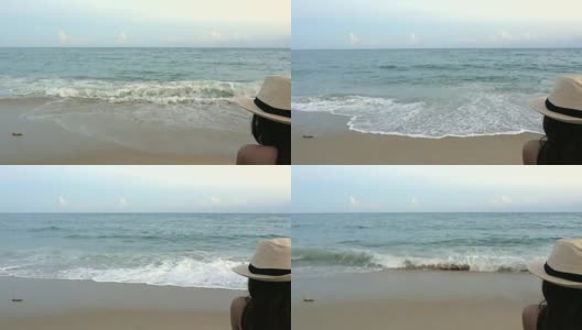 后视图幸福的女人在帽子坐在沙滩椅上热带海滩和蓝色的天空背景与海浪冲击海岸。独自女性旅行者享受户外暑假。高清在线视频素材下载