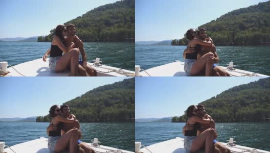 在阳光明媚的日子里，一对年轻的情侣坐在船头，对着摄影师摆姿势。幸福的情侣在船上共度时光，享受夏天的旅行。假期的概念。近距离高清在线视频素材下载
