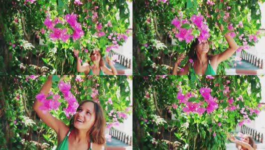 年轻美丽的女人走在粉红色的花的花园里，触摸和闻花和微笑。缓慢的运动。1920 x1080高清在线视频素材下载