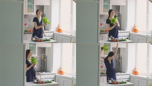 慢动作的滑稽女子烹饪舞蹈与绿色的莴苣，同时在厨房做饭在家高清在线视频素材下载
