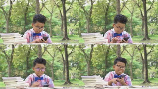 亚洲男孩在户外使用智能手机和看书。家庭观念、教育观念、小学观念、成长观念、学习观念、发展观念。4 k决议。高清在线视频素材下载