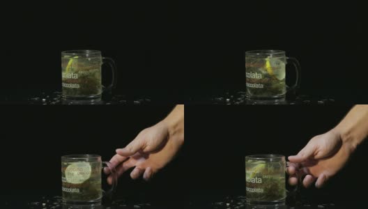 男人的手拿了一个盛着绿茶的玻璃杯。玻璃杯，里面有有机的干绿茶和柠檬片，在热水中漂浮。缓慢的运动。黑色背景高清在线视频素材下载