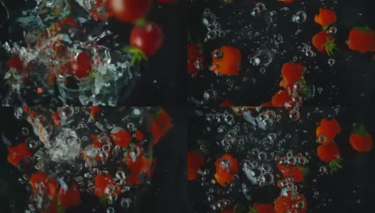 缓慢的运动。在黑色的背景下，几颗鲜嫩的红番茄带着绿色的尾巴坠入水中高清在线视频素材下载