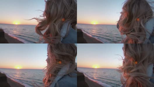 美丽的白种人卷发年轻女子日出或日落在海洋。风吹长了头发。她呼吸着海边的空气。自由的概念，生活的享受。缓慢的运动。近距离高清在线视频素材下载