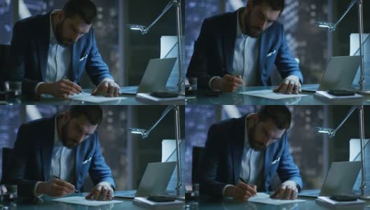 深夜商人在他的私人办公室里用笔记本电脑签署文件，可以看到大城市的窗户。高清在线视频素材下载