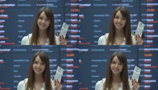 美丽的俄罗斯游客在机场面对镜头微笑，同时举着护照和登机牌高清在线视频素材下载