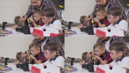 在现代舒适的游戏空间里，机械工程师帮助男孩用螺丝刀在桌子上组装机器人机器高清在线视频素材下载