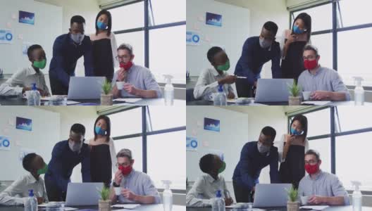 在现代办公室的会议室里，同事们戴着口罩一起使用笔记本电脑高清在线视频素材下载