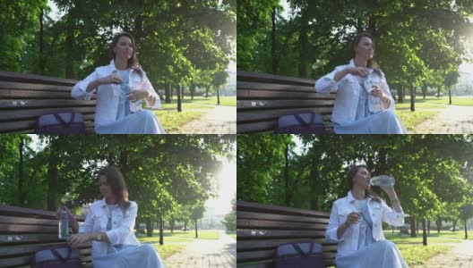 在公园里，一名穿着白色夹克的成年女子在喝瓶装水高清在线视频素材下载