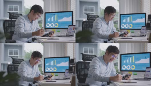 年轻有吸引力的亚洲泰国男子忙着工作多屏幕电脑或智能平板电脑在桌子上在家里的自由职业者数据分析师，数据科学的企业科学家。高清在线视频素材下载
