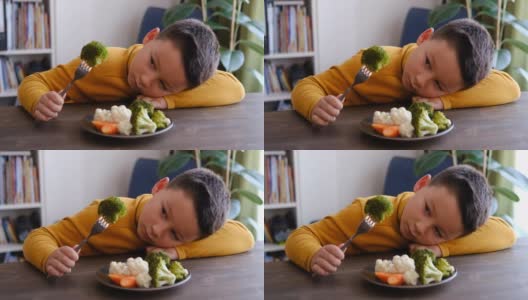 孩子对不得不吃蔬菜很不高兴。他的盘子里有许多蔬菜。他讨厌蔬菜。高清在线视频素材下载