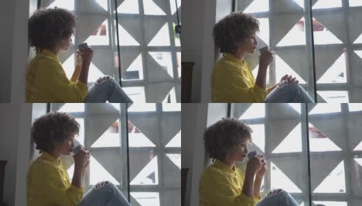 年轻女子坐在窗台上望着别处，在家里喝茶高清在线视频素材下载