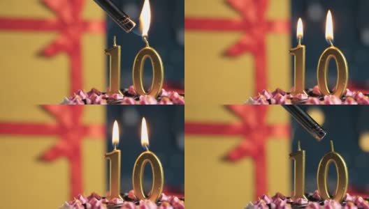 10号生日蛋糕用金色蜡烛点燃，蓝色背景的礼物用红色丝带绑在黄色盒子里。特写和慢动作高清在线视频素材下载