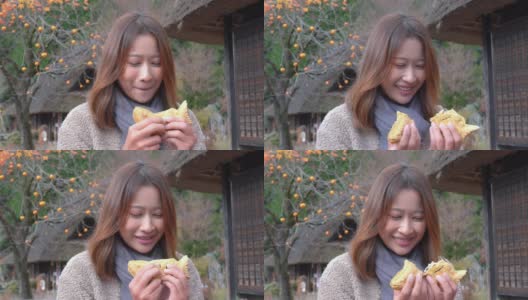 微笑的年轻亚洲女性游客喜欢吃传统的日本糕点与甜红豆沙在秋天日本古老的村庄。日本旅游和季节变化的概念。高清在线视频素材下载