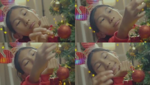 快乐的亚洲男孩穿着红色的毛衣和发带装饰圣诞树在晚上的时间在家里，节日的概念。高清在线视频素材下载