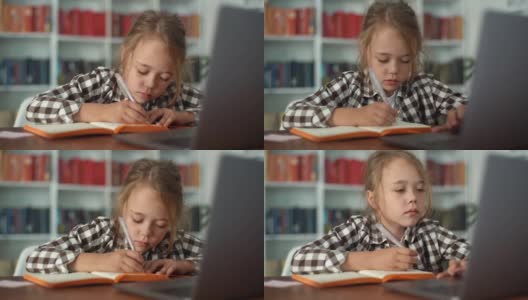 特写镜头是一名专注的小学女孩在做家庭作业，在笔记本上写笔记，看着笔记本电脑。高清在线视频素材下载