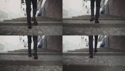 背面的男人穿着优雅的西装和黑色的鞋子沿着古老的街道爬混凝土楼梯，特写的人的脚爬慢动作楼梯。在街上与人擦肩而过的概念高清在线视频素材下载