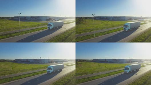 空中跟踪拍摄的白色卡车与半挂车连接移动通过工业仓库，农村地区。日落。高清在线视频素材下载
