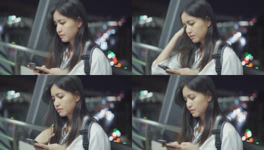 在泰国，一名年轻女子晚上站在走廊上使用智能手机。高清在线视频素材下载