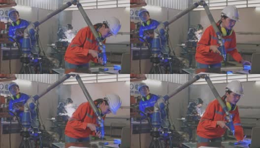 女工程师使用机械臂焊接钢板，并用笔记本电脑检查结果。一位男工程师正在用平板电脑检查工厂里的机械臂。后面的工人在焊铁，火花四溅。高清在线视频素材下载