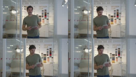 快乐的男性创意设计师靠在门面对摄像头，然后看着平板电脑在办公室高清在线视频素材下载
