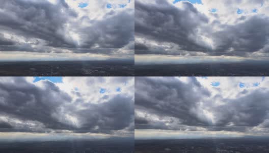 从高空的飞机窗口鸟瞰，远处的城市被暴雨前形成的蓬松的积云所覆盖高清在线视频素材下载