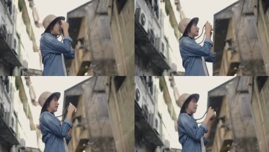 迷人的亚洲女性旅行者戴着复古软呢帽使用胶片相机拍照。享受暑假旅行。单独旅行的概念。高清在线视频素材下载