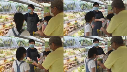 一位亚洲华人中年女性零售助理，建议并帮助一个家庭从超市的冷藏区选择蔬菜高清在线视频素材下载