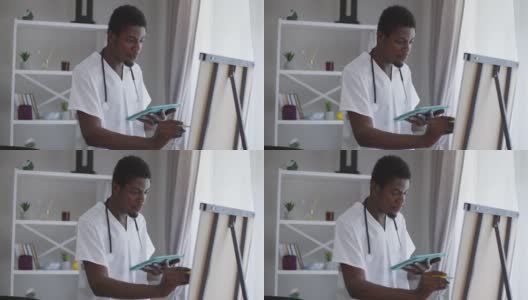 中镜头，聪明的非洲裔美国男性医生站在白板前，用记号笔书写。集中智慧的年轻人分析接种疫苗的副作用和效率。高清在线视频素材下载