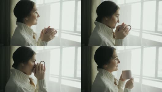 年轻漂亮的黑发女人，穿着毛衣，在窗边喝着咖啡高清在线视频素材下载
