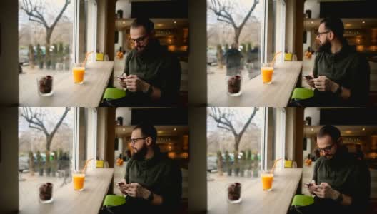 英俊的胡子男子在咖啡馆使用他的手机和享受健康饮料高清在线视频素材下载