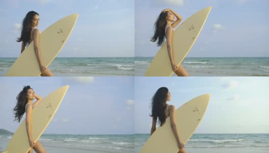 性感的亚洲女人在白色比基尼持有冲浪板和在蓝色的海和沙滩景观摆姿势。缓慢的运动。夏季，旅游和美丽的概念。高清在线视频素材下载