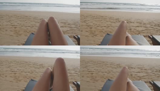 年轻女子躺在海边晒日光浴的床上。女性的腿在躺椅上放松和享受暑假在海洋海滩。一个度假胜地女孩的脚。近距离观点高清在线视频素材下载