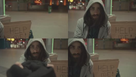 一个留着胡子和长发的无家可归的乞丐在空旷的街道上乞讨的慢动作。他旁边的纸板上写着“帮助我”。无家可归的概念,4 k。高清在线视频素材下载