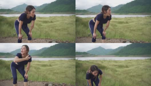 疲惫的年轻亚洲妇女在草地上跑步之间深呼吸的慢动作。汗流浃背的运动女性在草地上慢跑进行有氧训练。户外运动的生活方式和极限运动训练的概念。高清在线视频素材下载