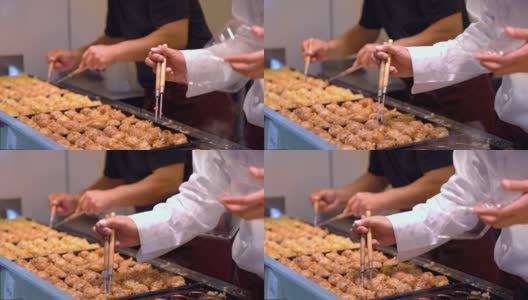 在日本的街头小吃市场上，大厨在夏季的节日期间，用高清慢镜头近距离拍摄的日本小吃章鱼烧。男子烹饪什锦传统日本肉丸。高清在线视频素材下载