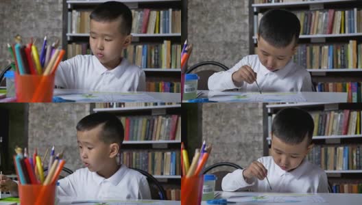 年轻专注的亚洲孩子在纸上画画，坐在桌子后面，男孩做作业，书架的背景高清在线视频素材下载